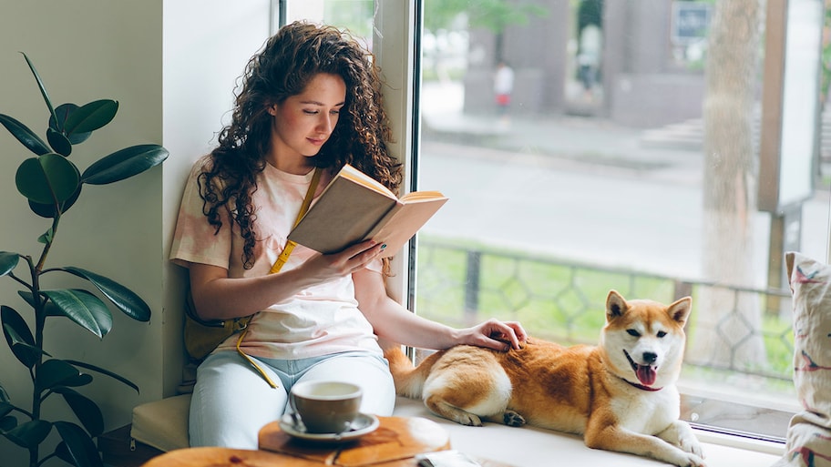 woman reading a book with her dog by a window